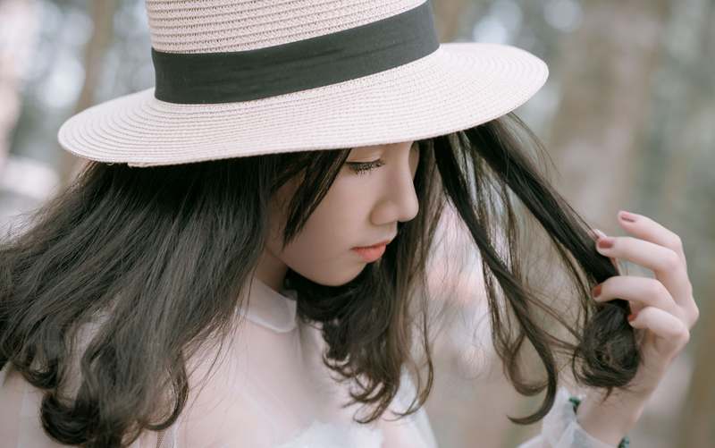 Woman wearing a wide-brimmed sun hat with soft waves, standing in golden-hour sunlight